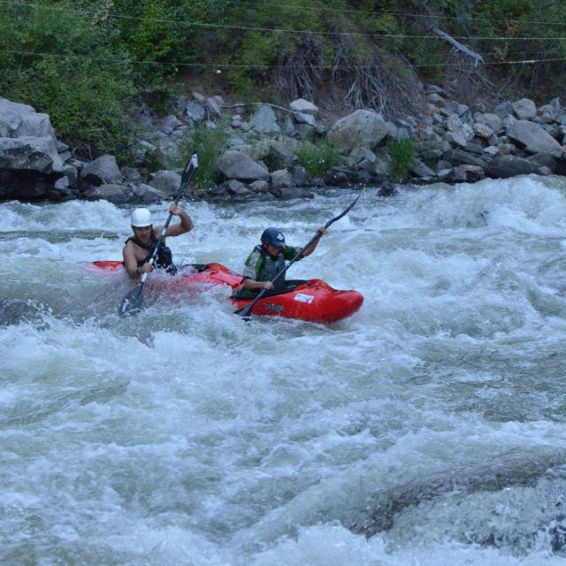 Kayaker in a red boat paddling through rapids