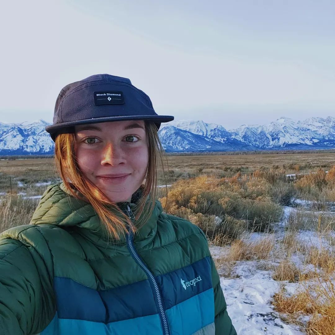 Staff member wearing a cap with snowy mountains behind