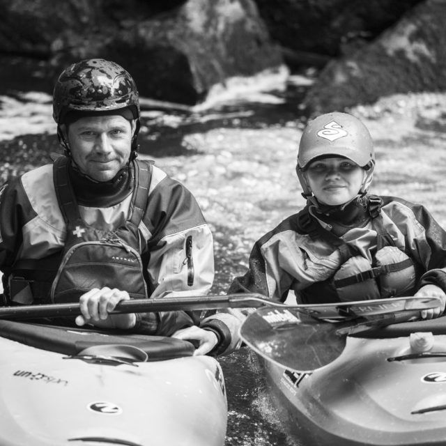 Two helmeted paddlers beside whitewater rapids