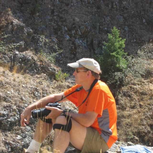 Staff member wearing a cap beside a rocky hillside