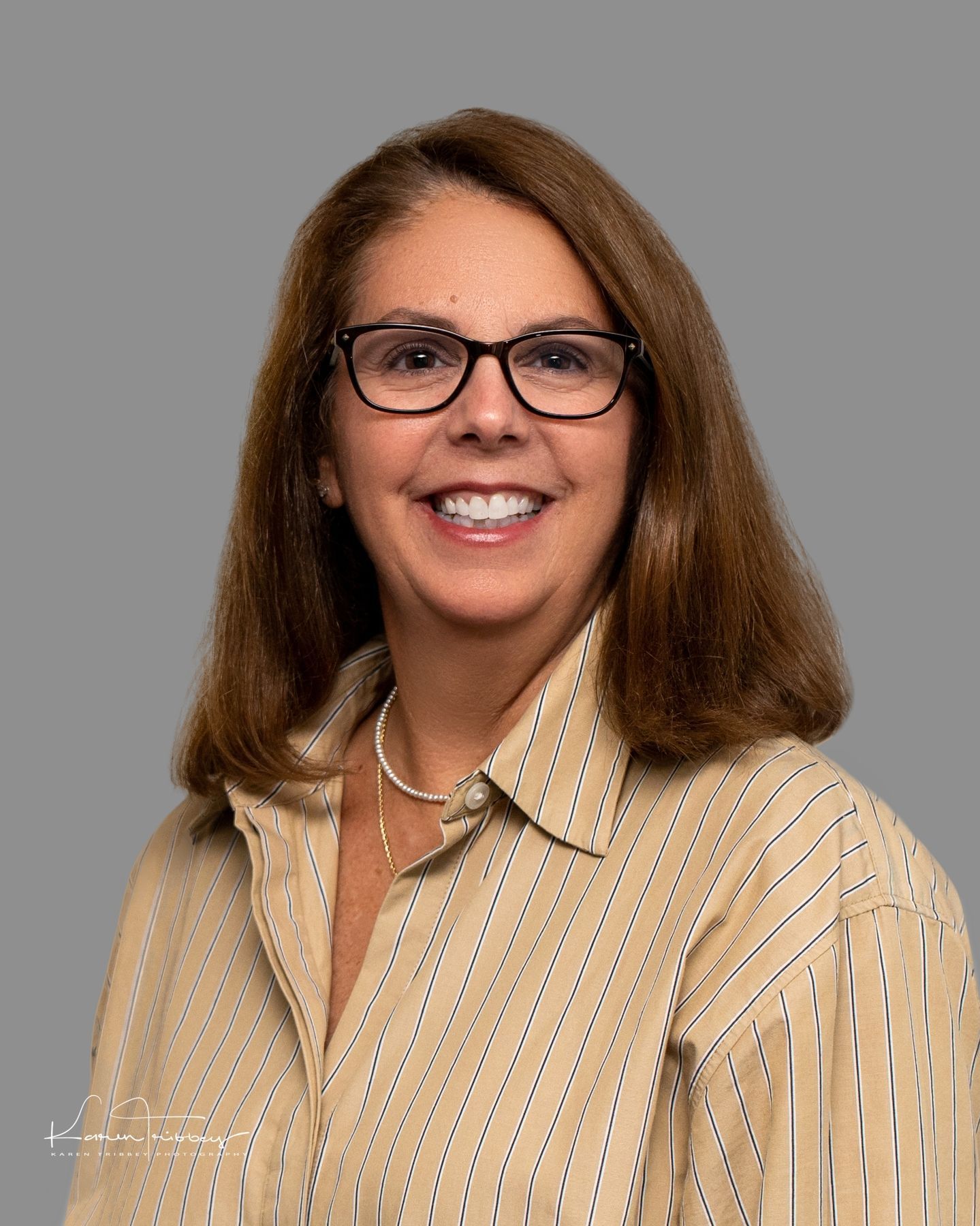 A woman wearing glasses and a striped shirt is smiling for the camera.