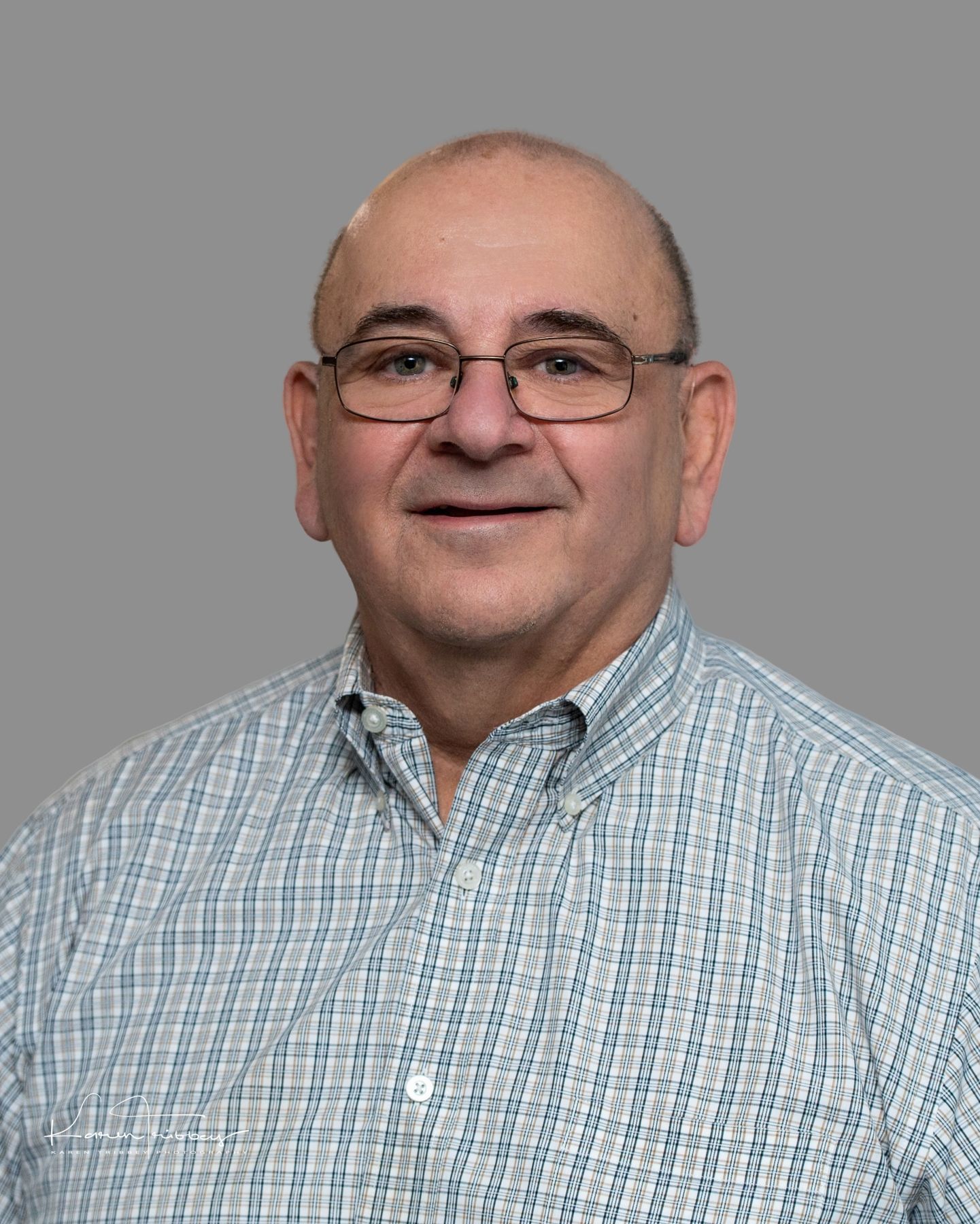 A man wearing glasses and a plaid shirt is smiling for the camera.
