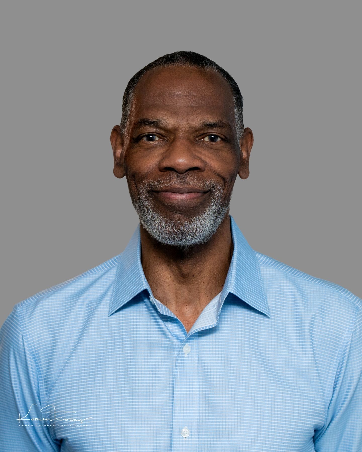 A man with a beard is wearing a blue shirt and smiling.