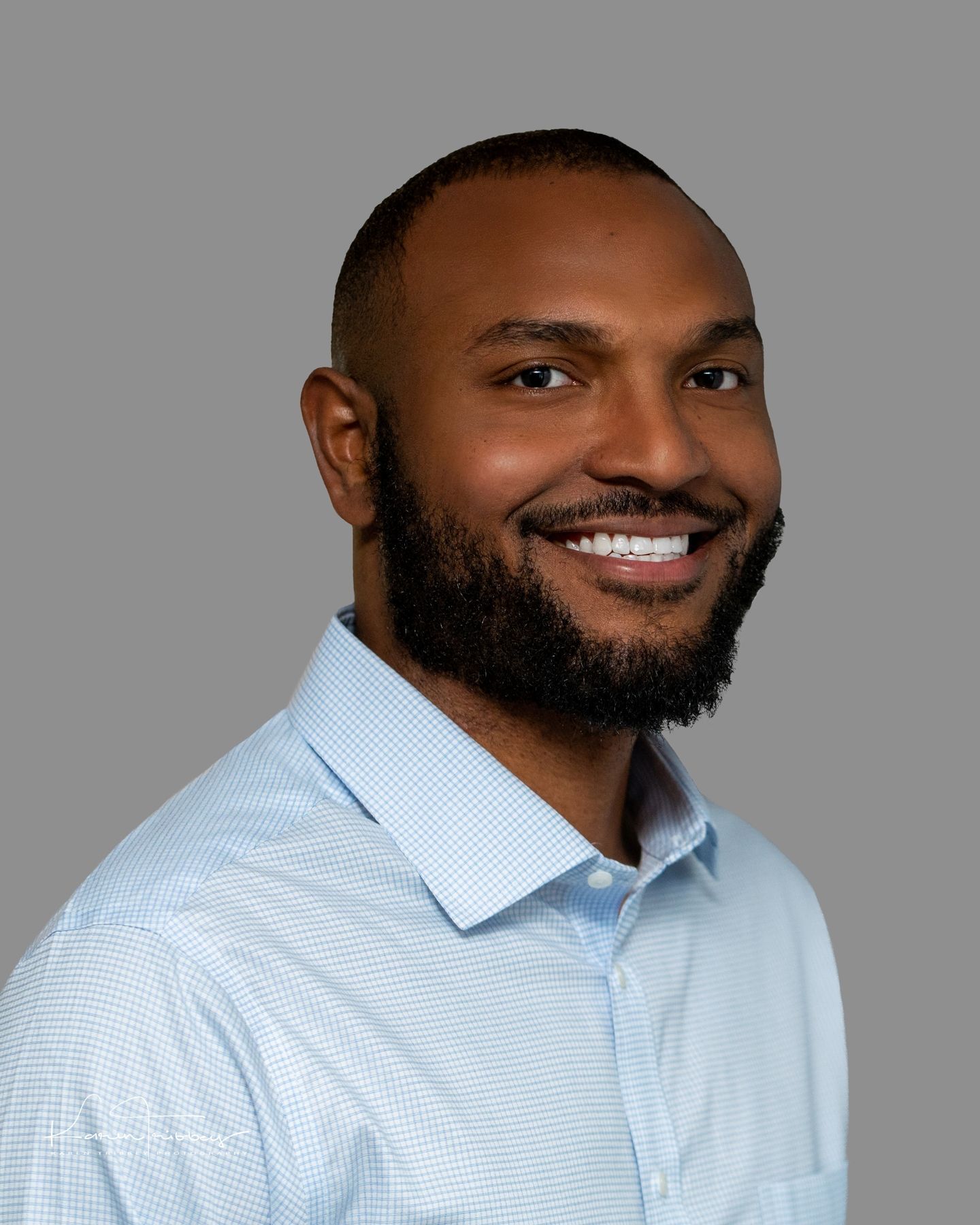 A man with a beard is smiling for the camera while wearing a blue shirt.