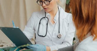 A doctor is talking to a patient while looking at a clipboard.