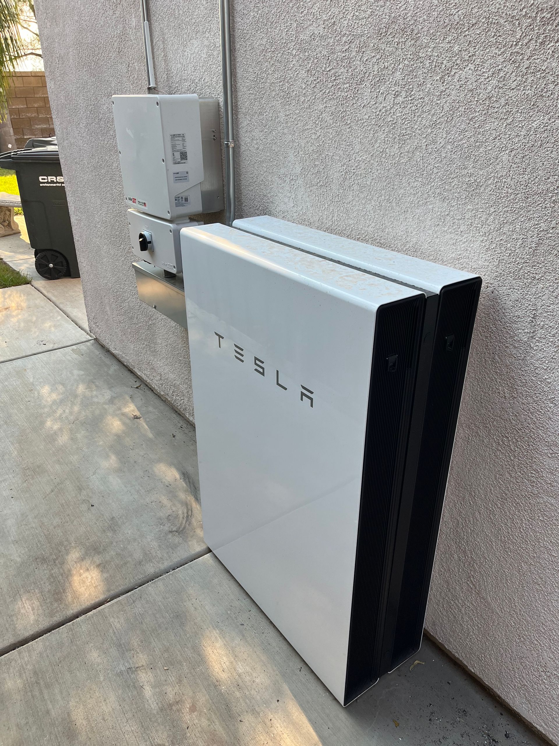 Tesla Powerwall battery system mounted on an exterior wall next to electrical components.