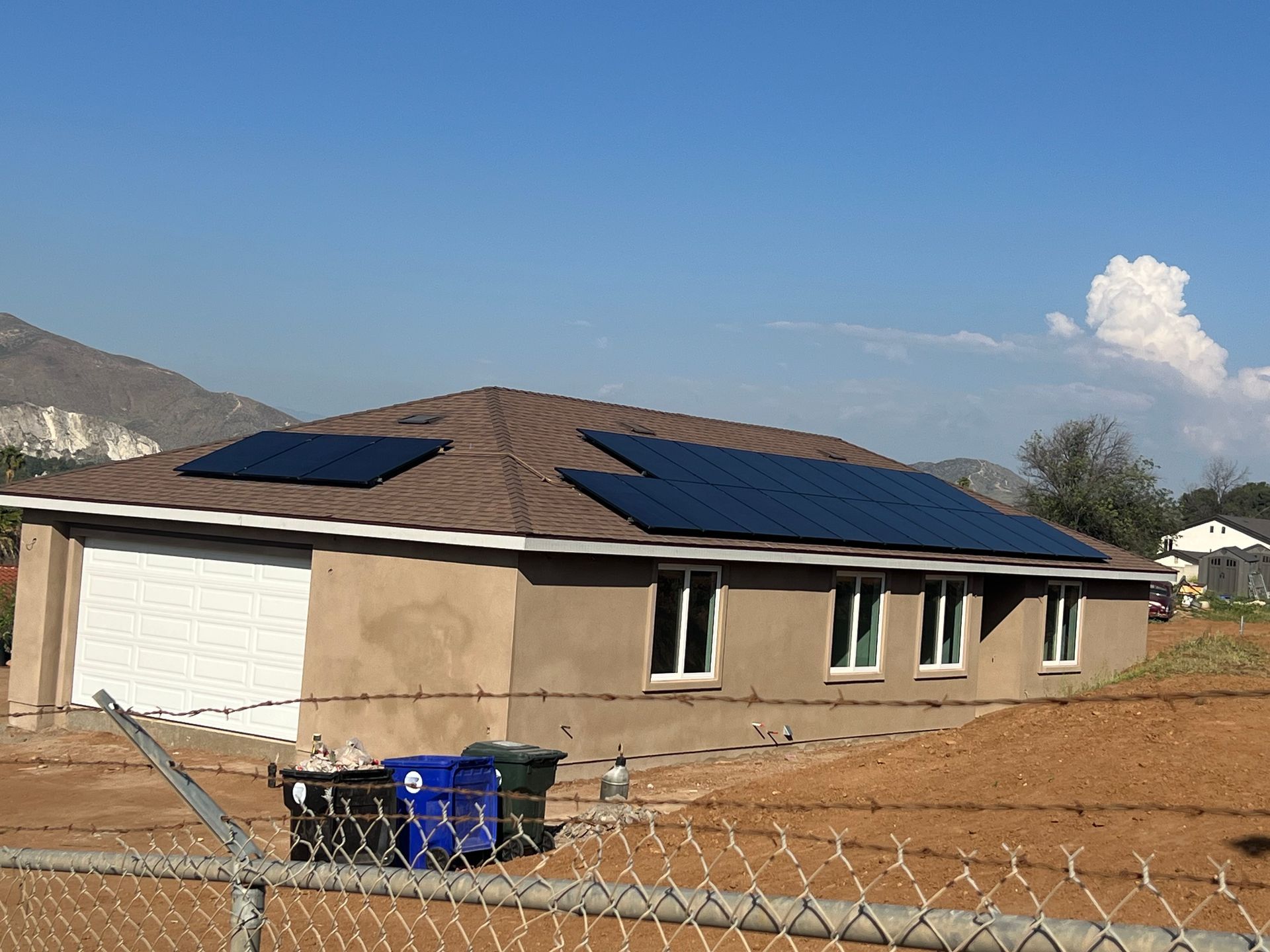 Two workers installing solar panels on a house roof with a mountain backdrop.