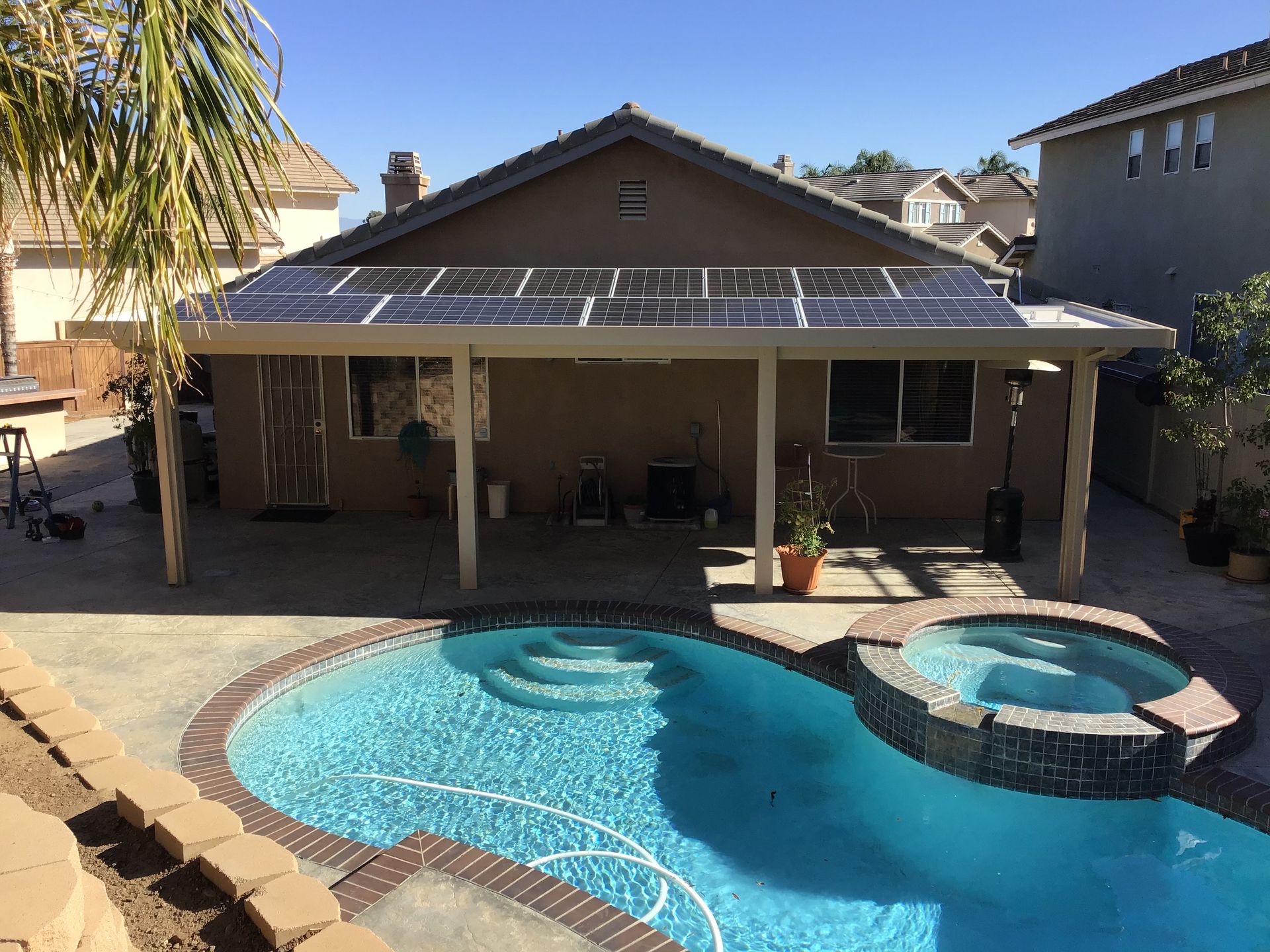 Backyard with a pool and spa, covered patio with solar panels on roof. Sunny day.