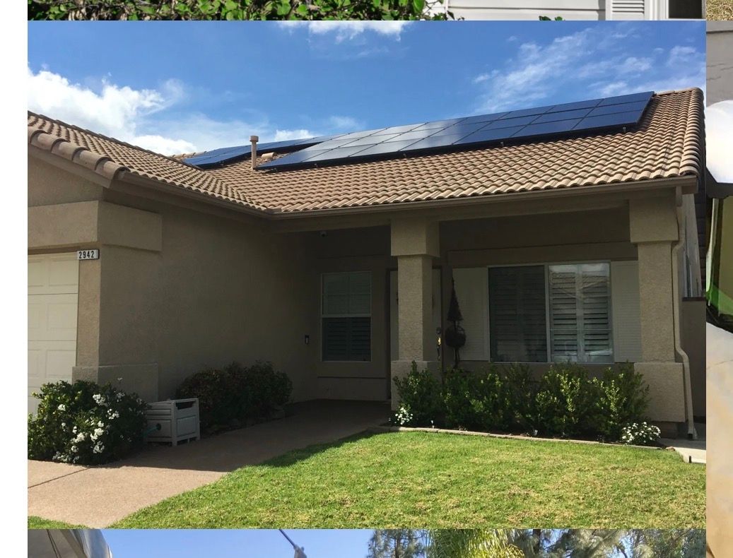 House with solar panels on a brown roof, beige exterior, green lawn, and blue sky.