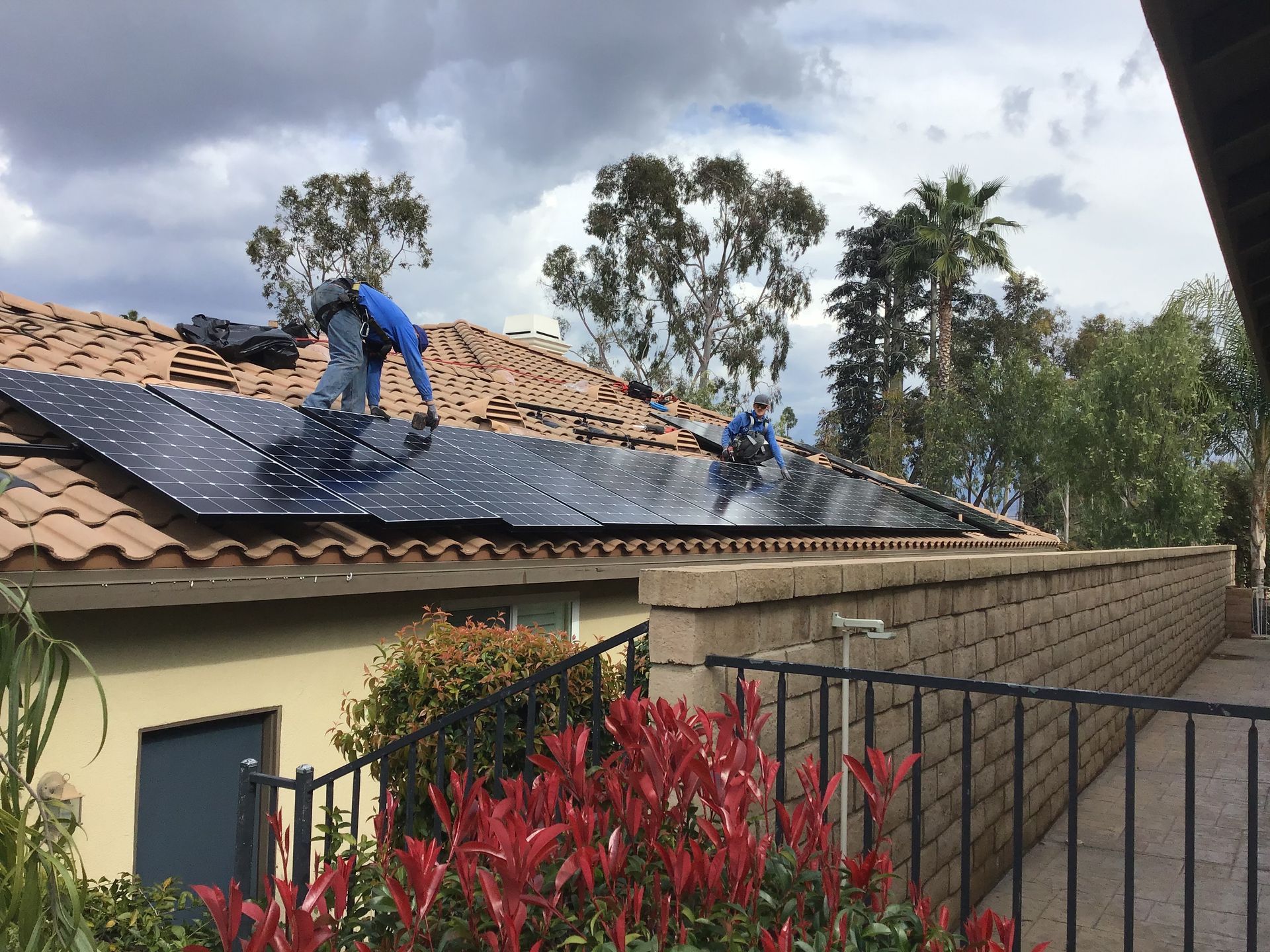 Workers installing solar panels on a rooftop, wearing safety gear. Blue sky overhead.