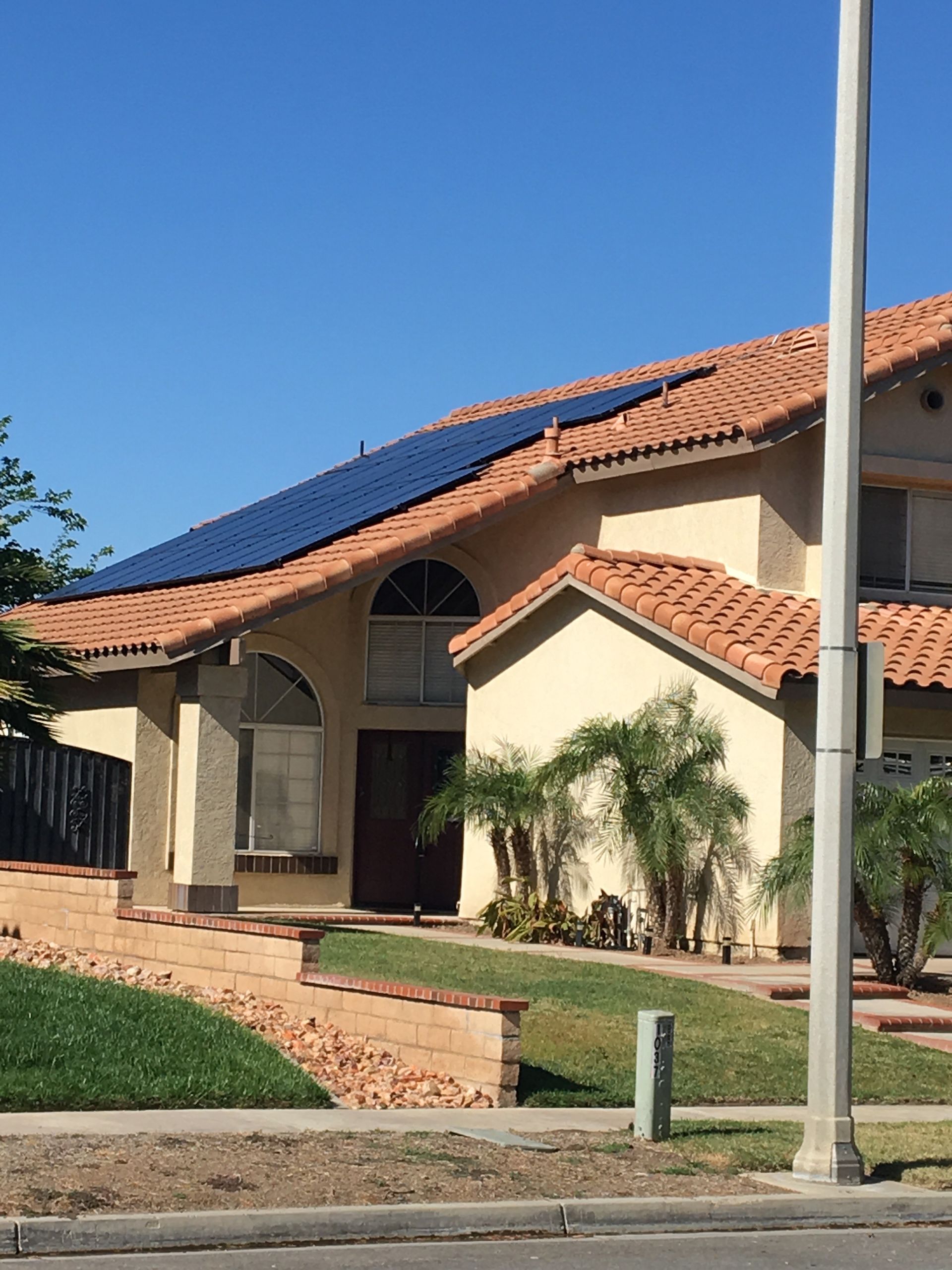 Roofer installing solar panels on a residential roof under a bright blue sky.