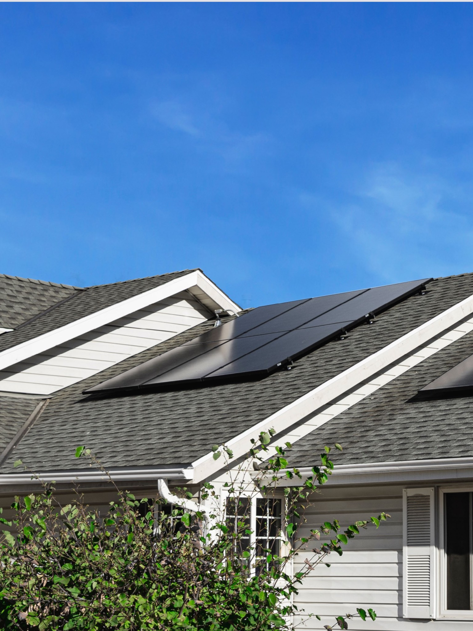 House with solar panels on roof against a bright blue sky.