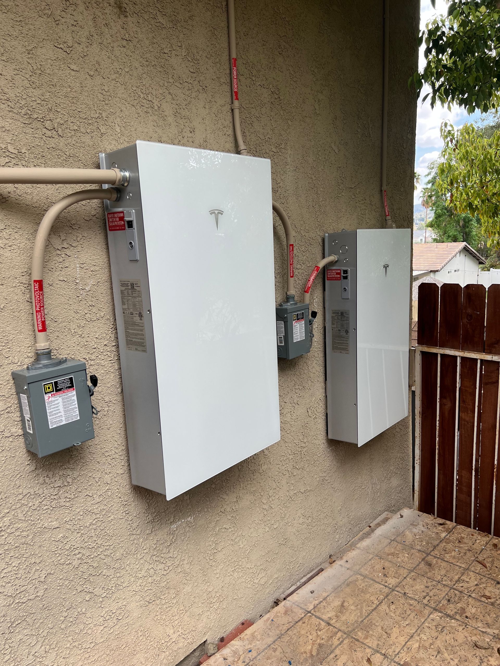 Two white rectangular Tesla Powerwall batteries mounted on a stucco wall outside a building.