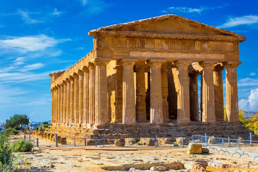 Il gruppo di turisti si è riunito accanto a un furgone nero in un soleggiato punto panoramico sulla costa, con vista sul mare blu e sulle colline rocciose.