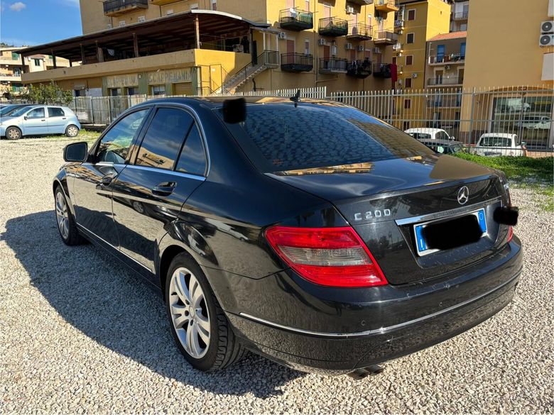 Una berlina di lusso nera parcheggiata al crepuscolo su una strada cittadina bagnata, con le vetrine illuminate sullo sfondo.