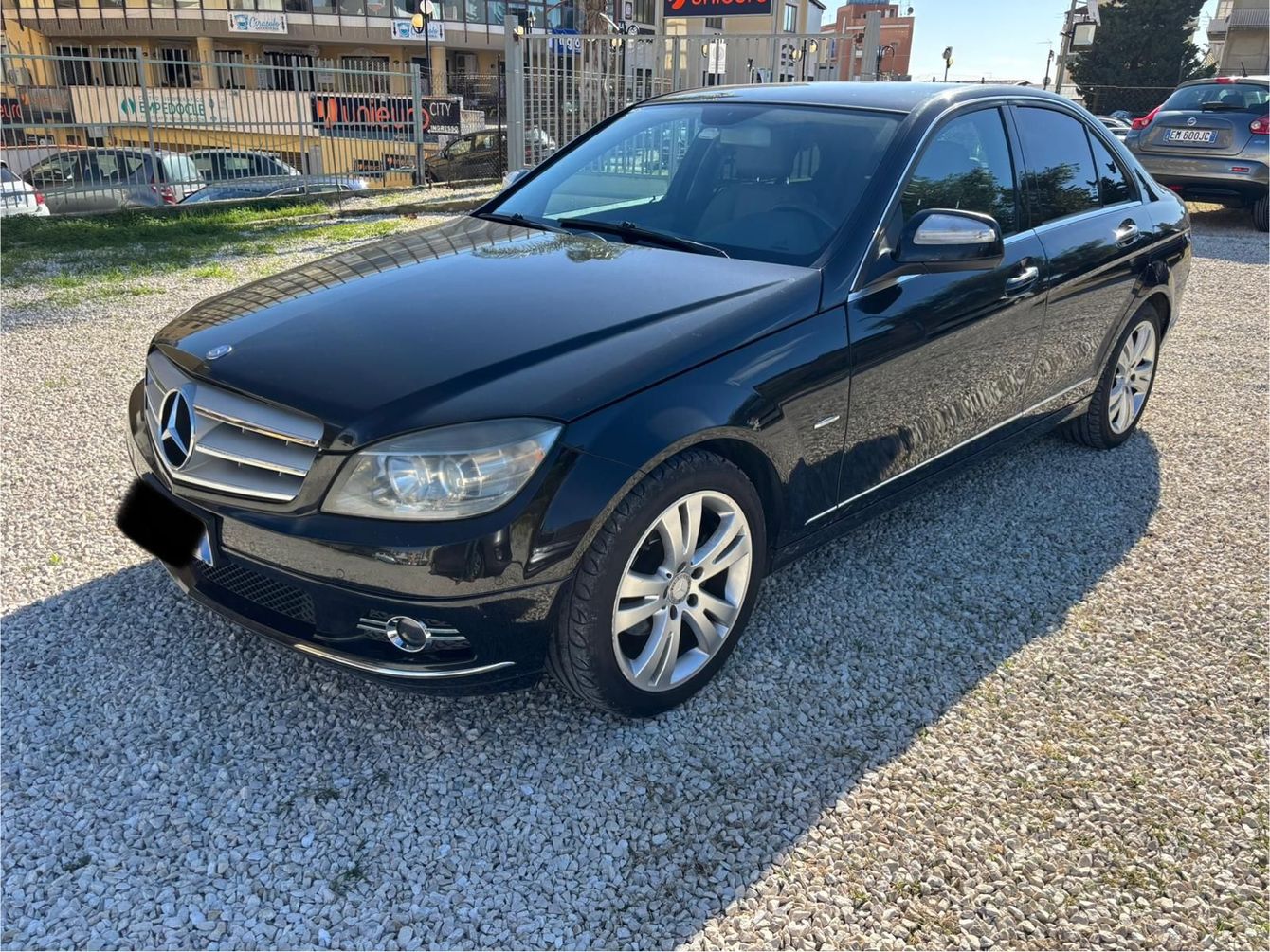 Una berlina di lusso nera parcheggiata di notte su una strada bagnata, di fronte a edifici illuminati.