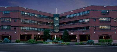 Red brick church building at dusk with a cross-topped glass center tower and landscaped entrance.