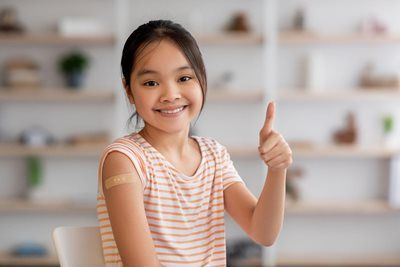Smiling child giving a thumbs-up in a bright room with shelves in the background