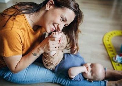 Woman in an orange shirt cuddles a baby on a blue blanket, smiling in a cozy indoor setting.