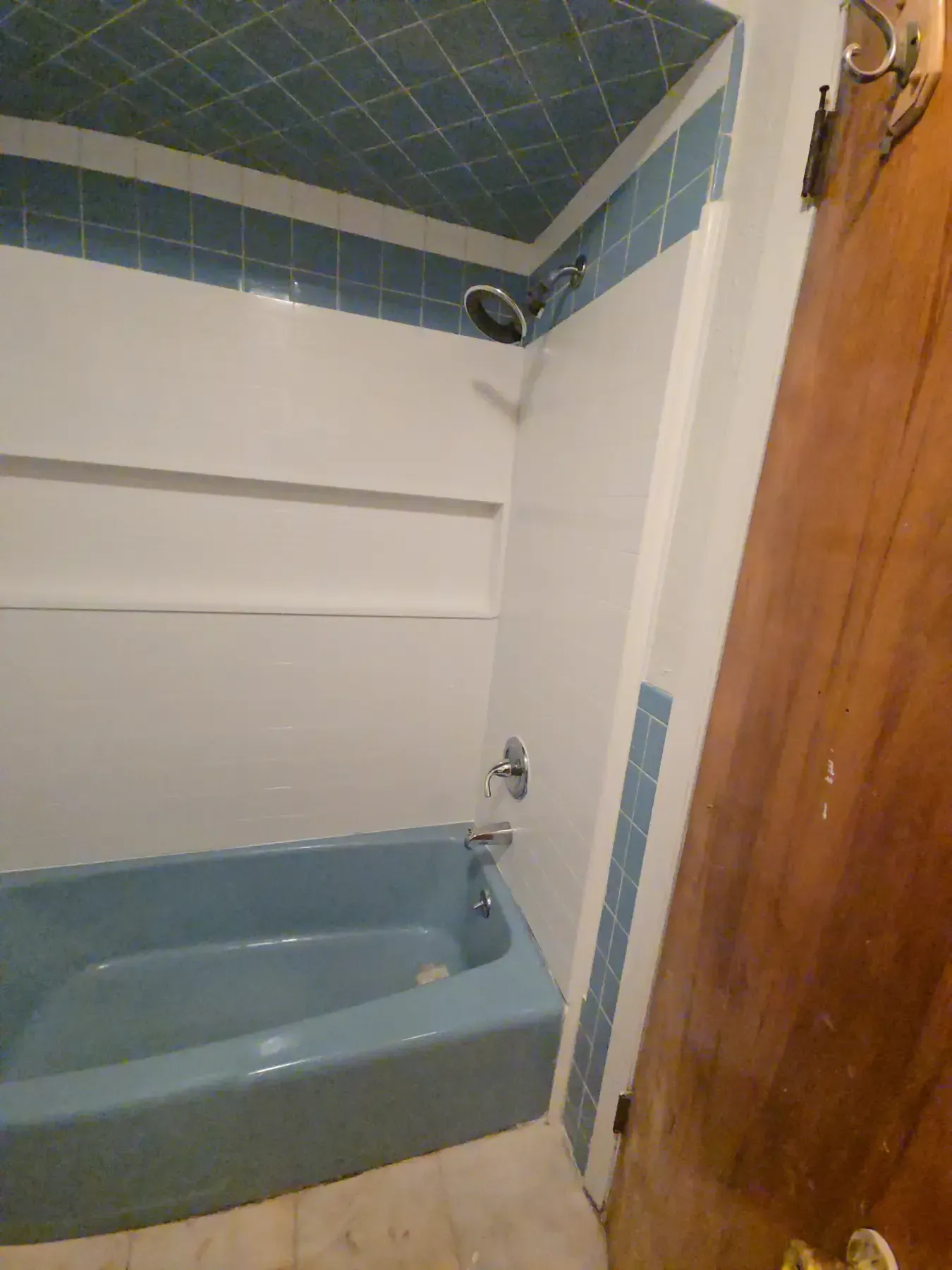 Small bathroom with blue bathtub, tiled walls, and a wooden door.