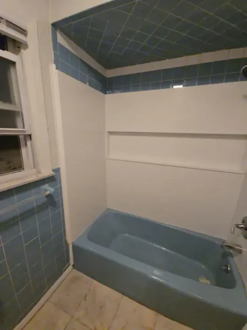 Blue bathtub in a small tiled bathroom with a window and white walls.