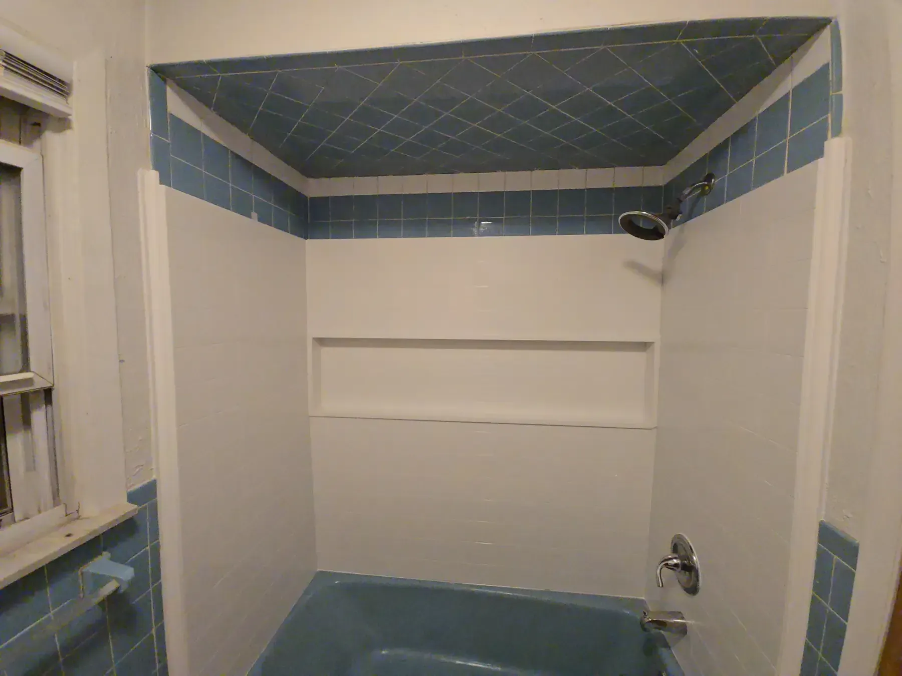 Blue-and-white tiled bathtub and shower stall with a built-in shelf and showerhead