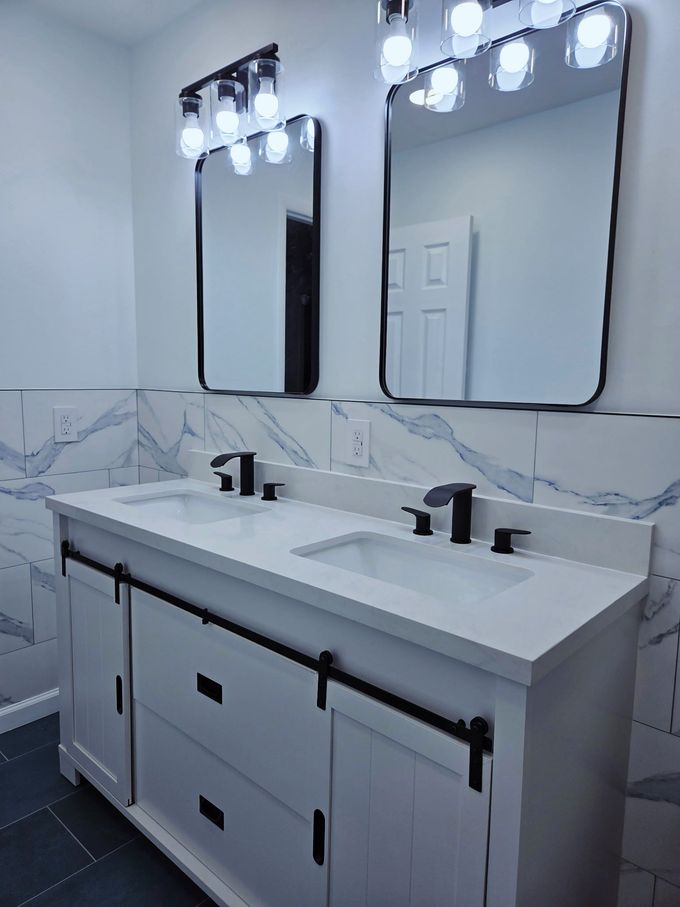 Modern bathroom vanity with double sinks, black faucets, and two illuminated mirrors