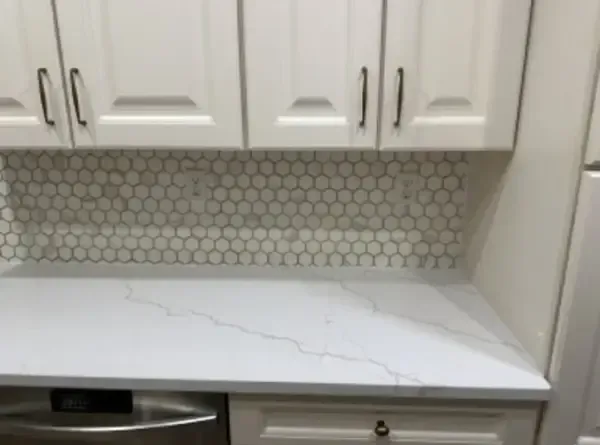 White kitchen countertop with a visible crack beneath white cabinets and hexagon tile backsplash