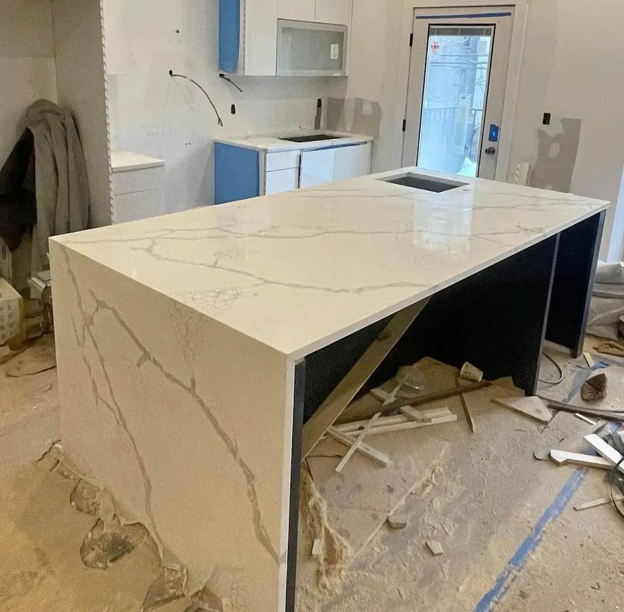 Kitchen with a large white stone island under construction, debris and tools scattered on the floor.