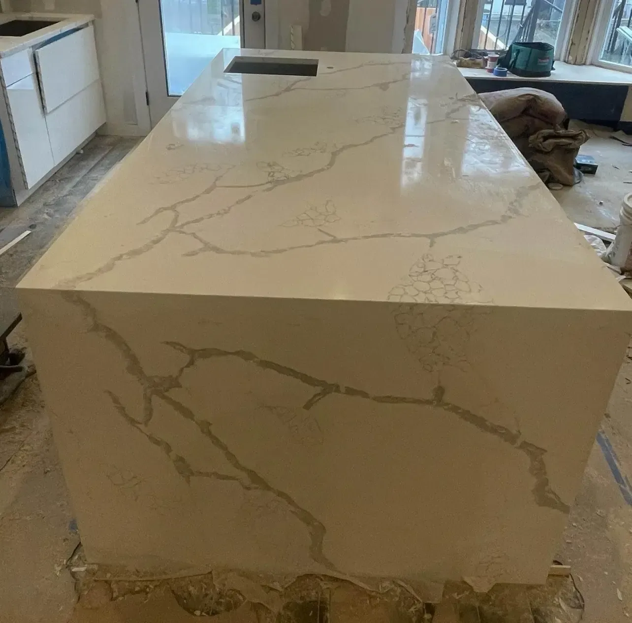 Large white marble-look kitchen island countertop in a kitchen, with veined stone and unfinished base below.