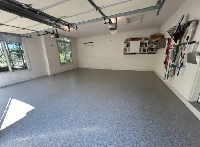 Empty garage with gray floor, white walls, windows, open garage door tracks, and wall-mounted tools.