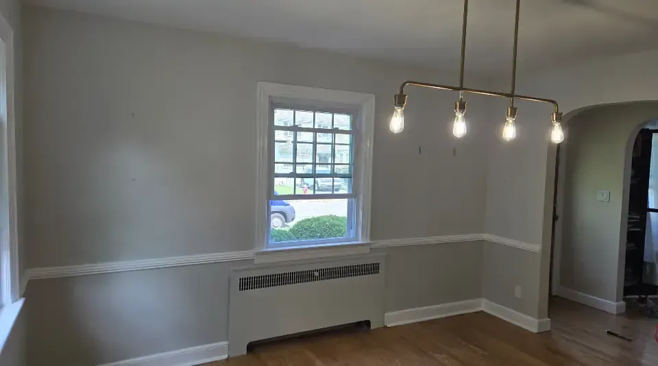 Empty dining room with white walls, wood floor, window, radiator, and hanging light fixture