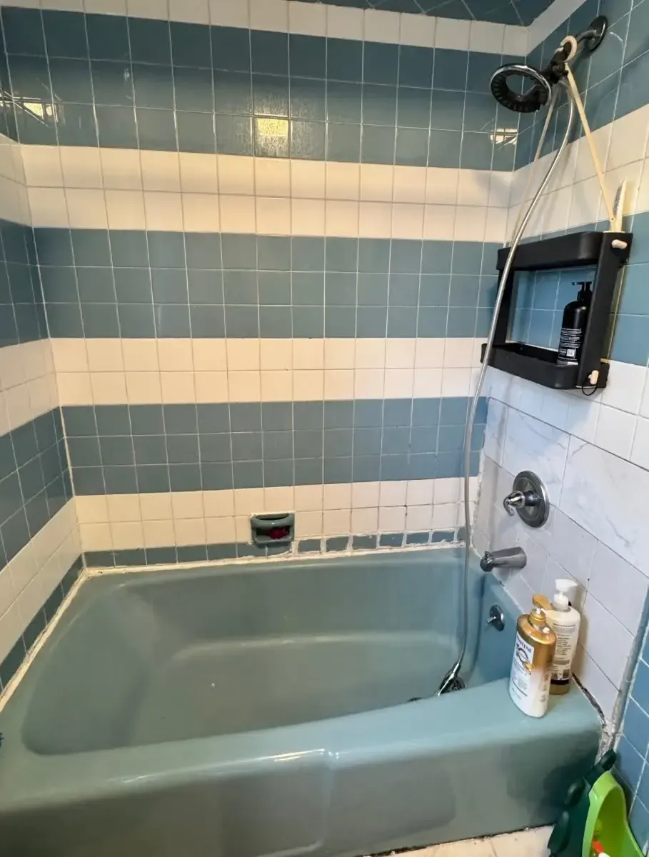 Small bathroom with a blue bathtub, tiled walls, showerhead, and wall-mounted TV above the tub.