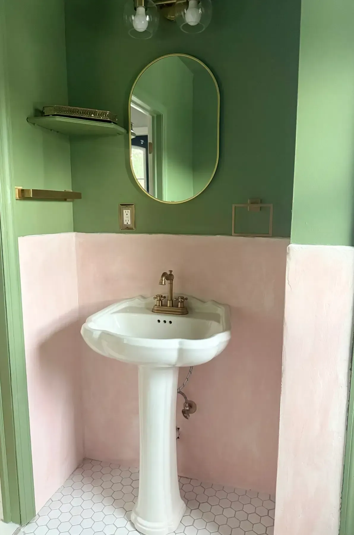 Small bathroom sink with oval mirror, green walls, and pink lower wall tiles.