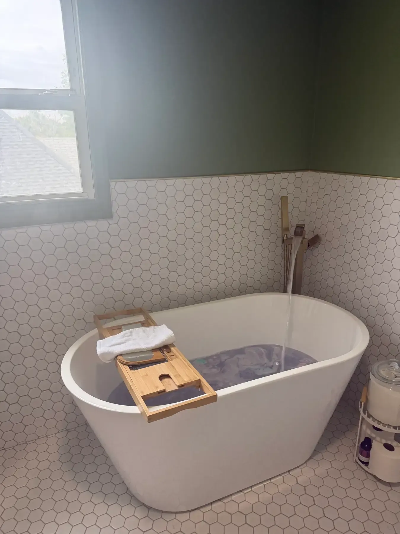 Modern bathroom with a freestanding tub, wooden bath tray, and a small bucket beside the wall.
