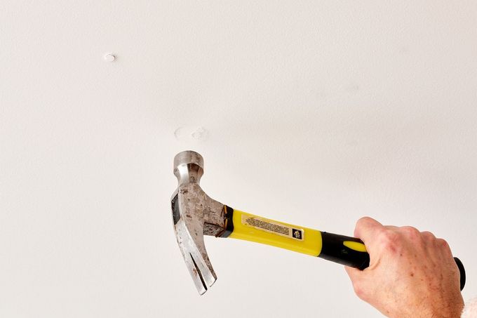 Hand holding a yellow-and-black hammer, striking a nail in a wall