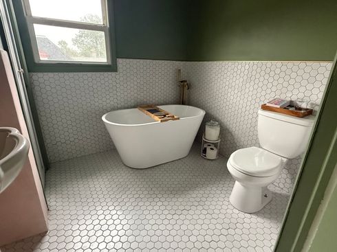 Small bathroom with a white tub, toilet, hex tile floor, and green walls.