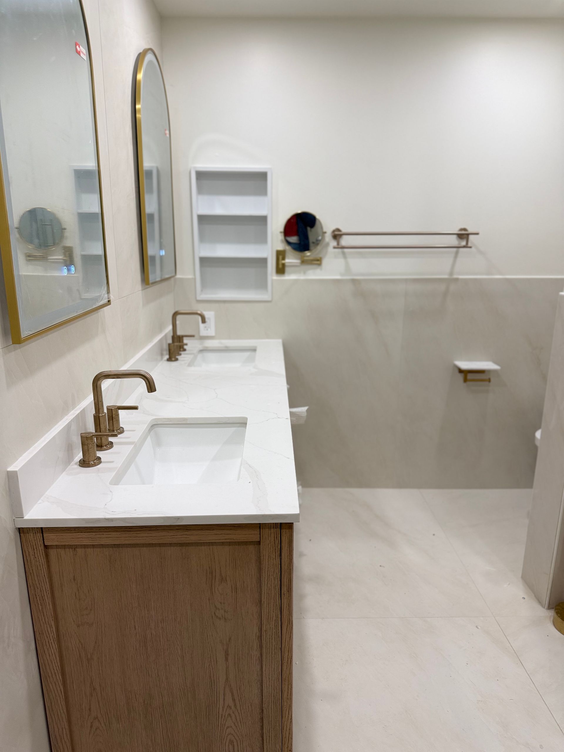 Accessible bathroom with double sinks, gold-framed mirror, shelves, and grab bar near the toilet.