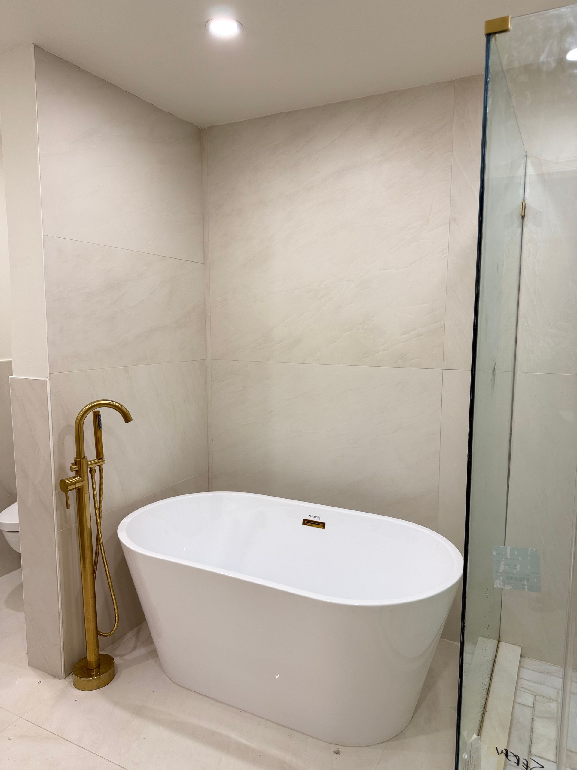 Modern bathroom with a white freestanding tub, brass faucet, and glass shower enclosure