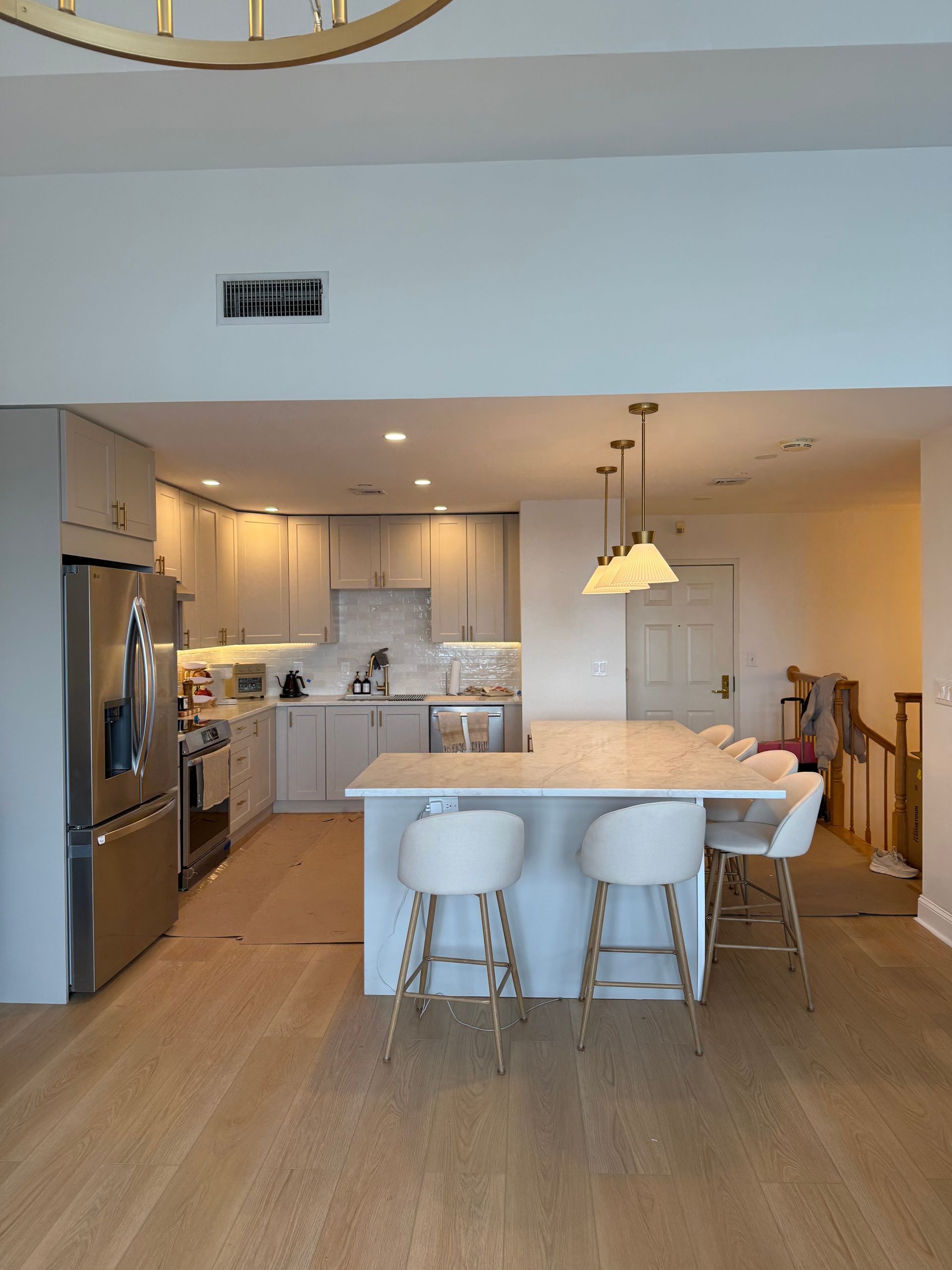 Open-concept kitchen with white island, pendant light, stainless appliances, and light wood flooring