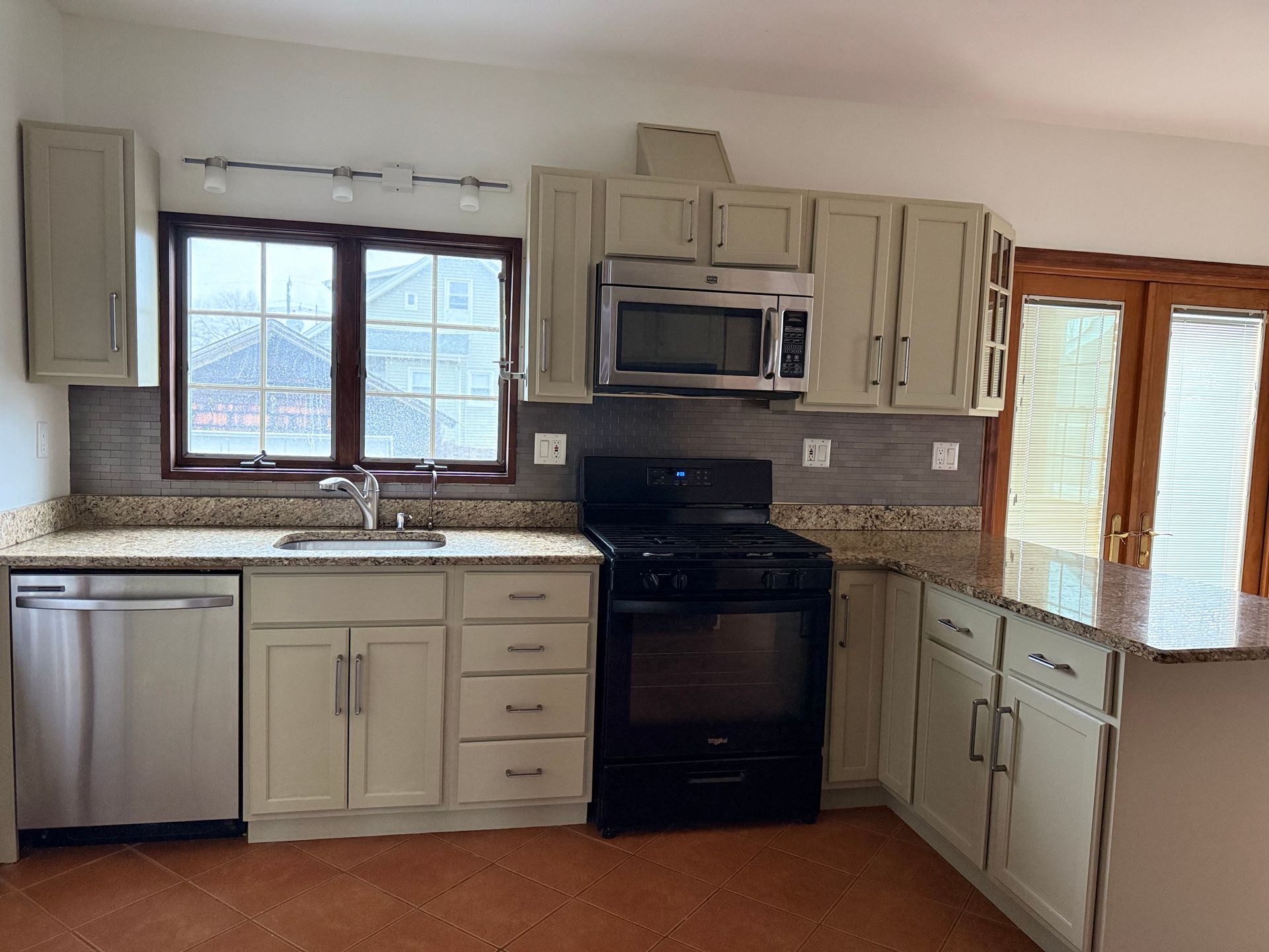 Bright kitchen with white cabinets, black stove, stainless dishwasher, granite counters, and window over sink