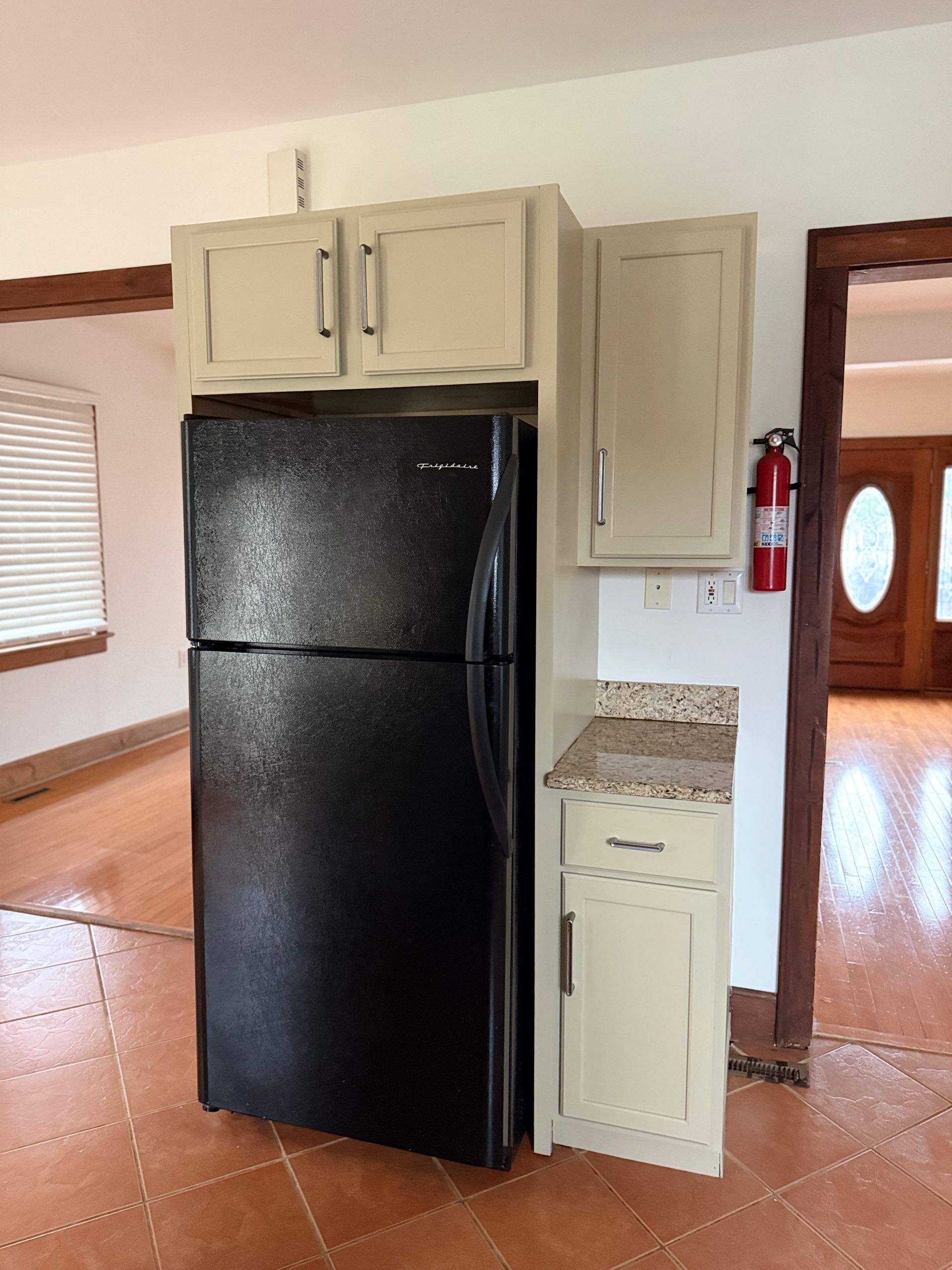 Kitchen with black refrigerator, beige cabinets, and wood flooring in a bright home interior
