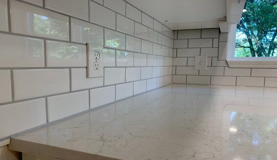 White subway-tile kitchen backsplash and marble countertop near a window with trees outside