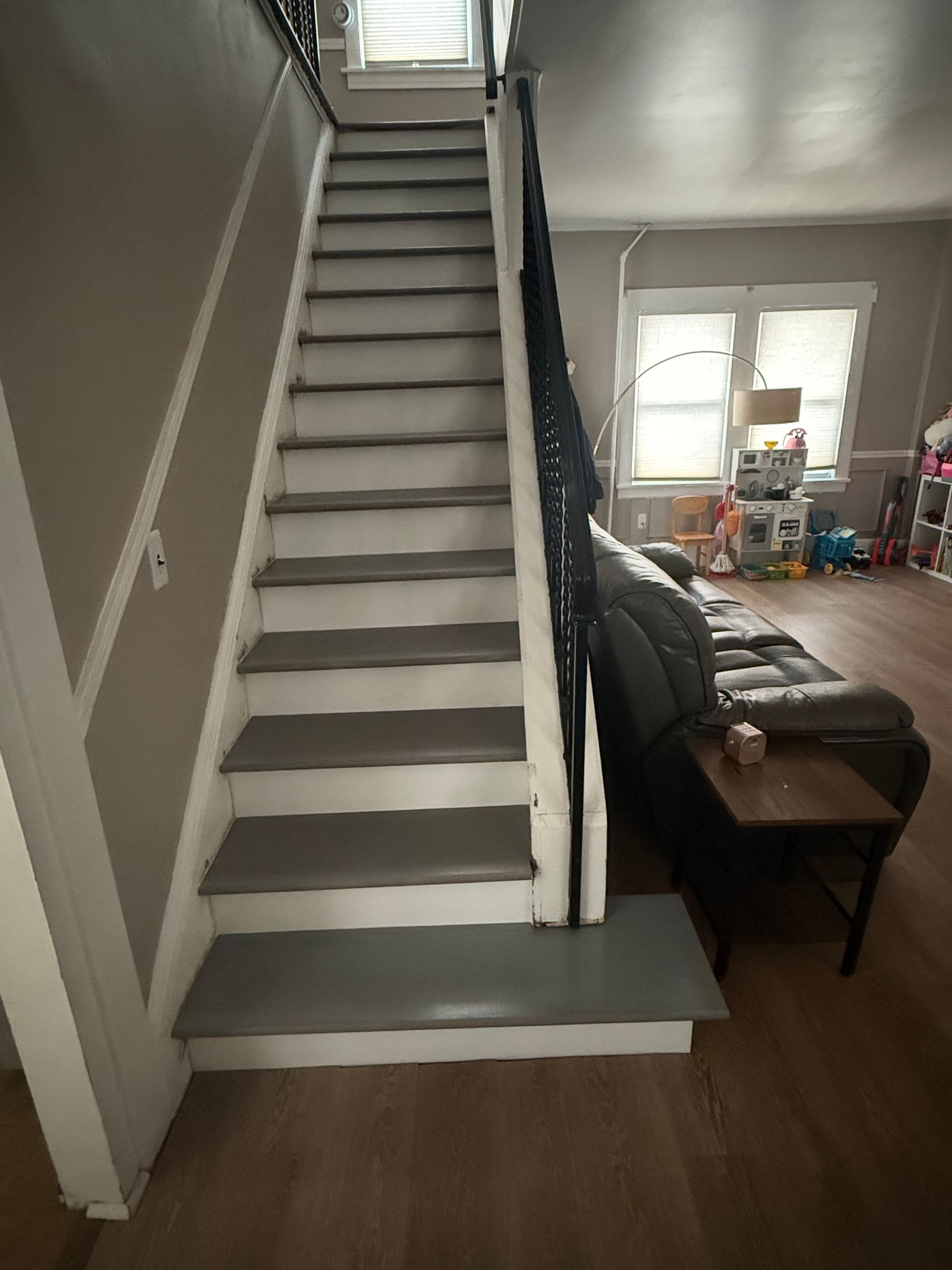 Carpeted staircase in a living room, painted gray and white, with a couch and window beside it.