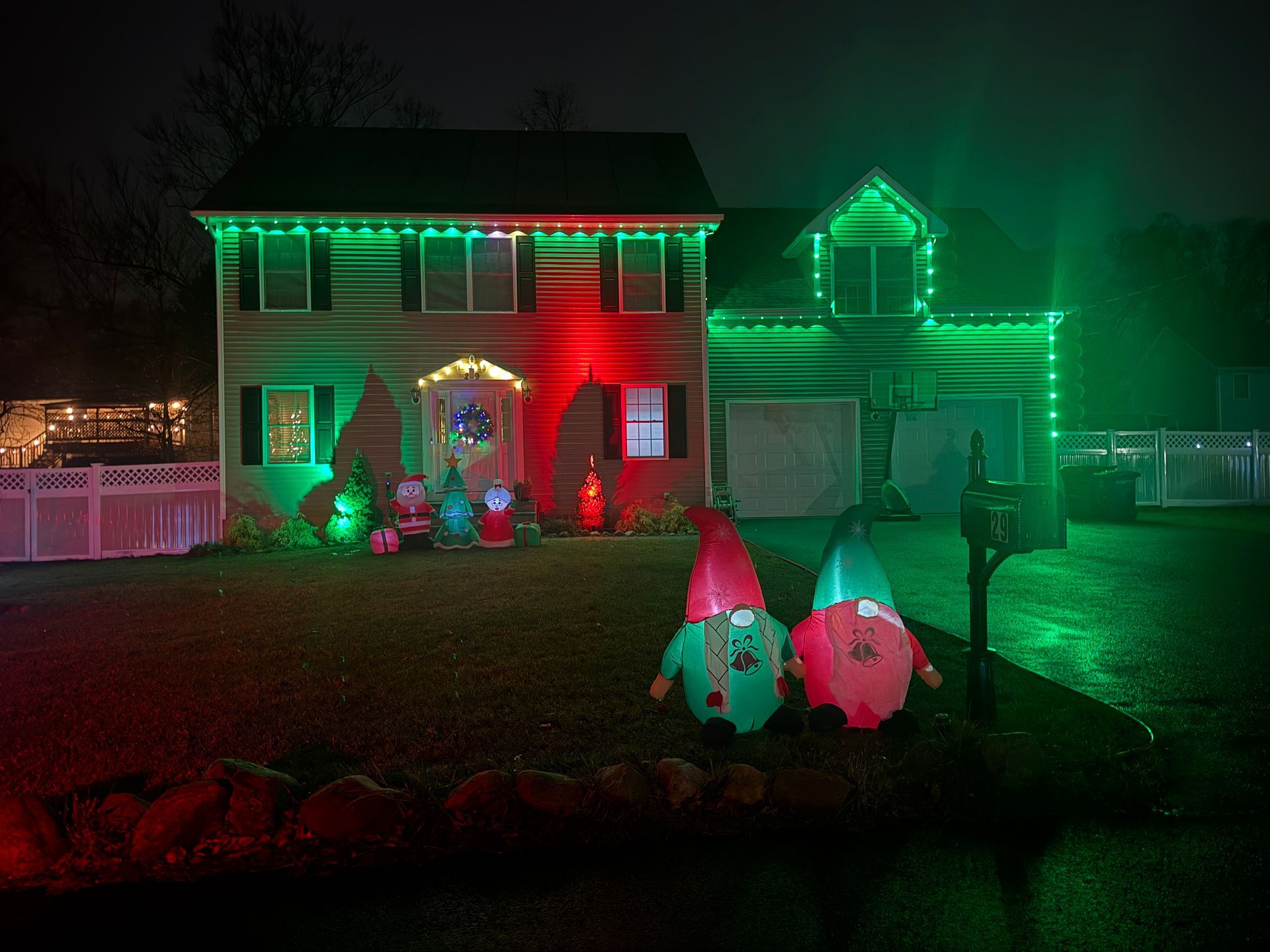 House and yard decorated with green and red Christmas lights, with inflatable holiday figures in front