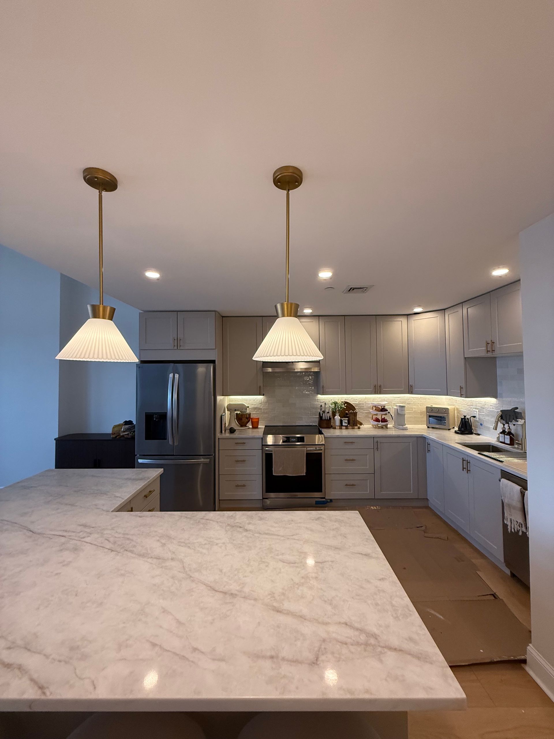 Modern kitchen with large marble island, pendant lights, stainless appliances, and light gray cabinets