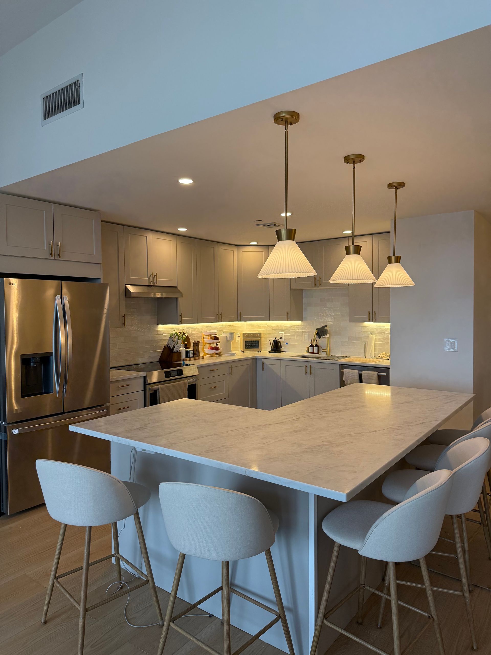 Modern kitchen with a large island, white stools, pendant lights, and stainless steel appliances