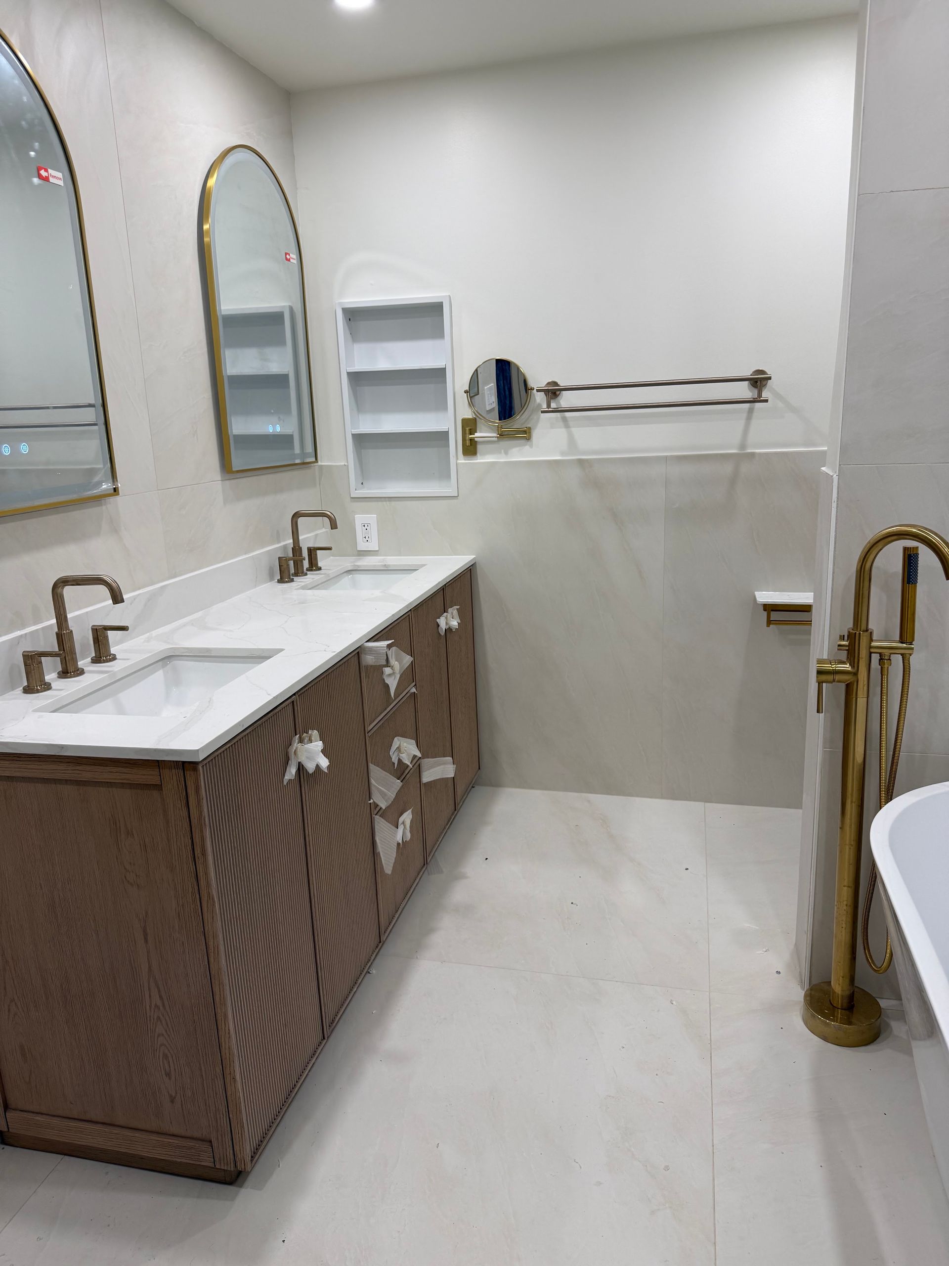 Modern bathroom with double sinks, wall mirrors, white tile, and brass fixtures