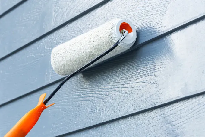 Paint roller applying light blue paint to horizontal siding