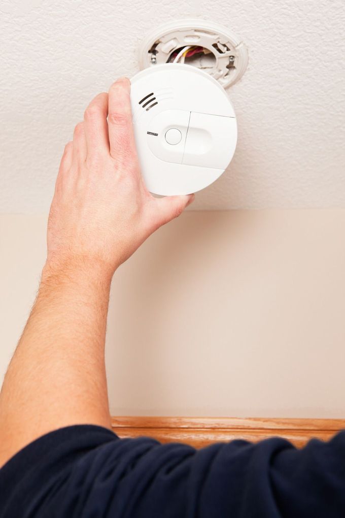 Hand installing a white smoke detector on a ceiling mount
